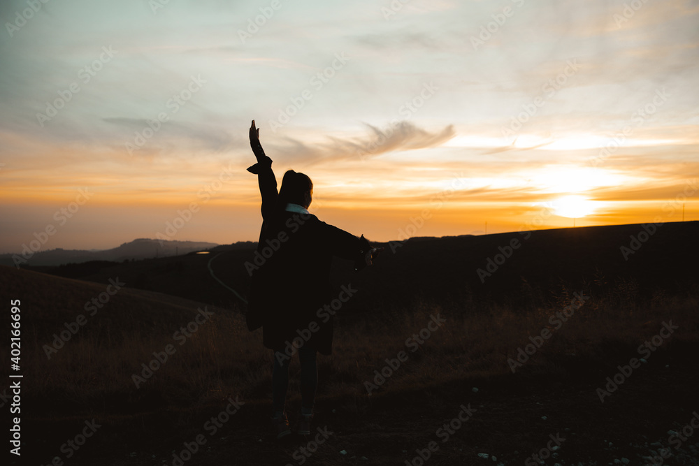 young woman in running up on top of mountain summit at sunset,, raises arms into air, happy and drunk on life, youth and happiness