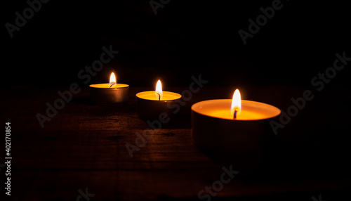 Three lighted tea wax candles on a wooden table on a black background