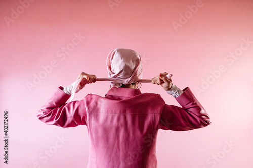 Woman from behind tying a pink scarf on her head, cancer patient.