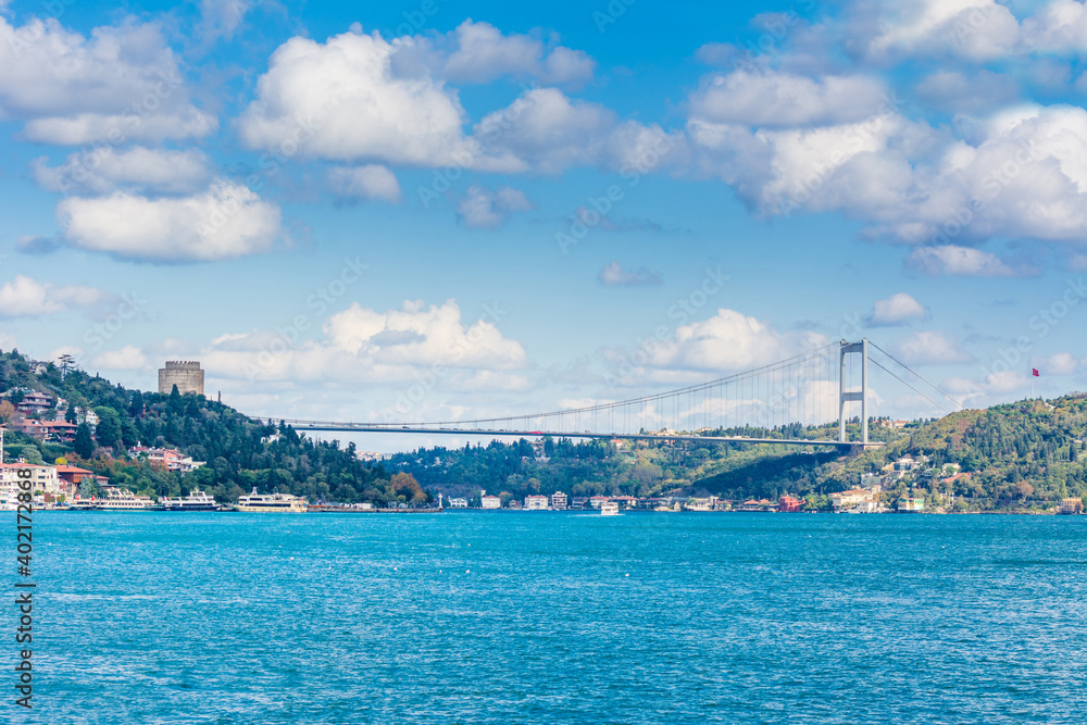 Modern builings and Rumelian Castle, and Fatih Sultan Mehmet Bridge across the Bosphorus strait in Istanbul Turkey from ferry on a sunny day with background cloudy sky