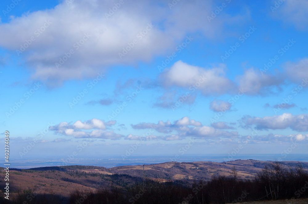 Panoramic view of gray autumn mountains covered with forest with fallen leaves under blue sky with white clouds in autumn day
