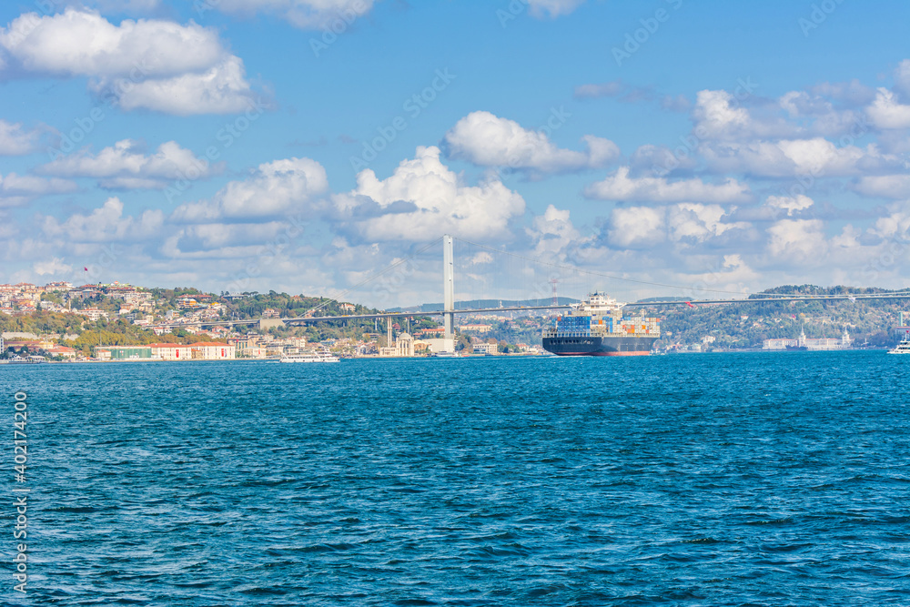 Merchant ship passing through Bosphorus  Bridge with background of Bosphorus strait on a sunny day with background cloudy blue sky and blue sea in Istanbul, Turkey. Blue Turkey concept.