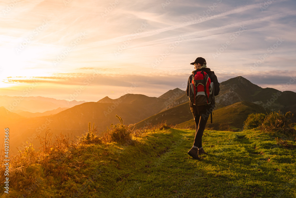 Traveler woman with backpack doing a mountain hike and watching a beautiful sunset. sports and adventure.