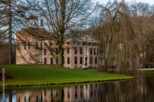Barren winter trees on green meadow grass with Rosendael castle in the background and reflection of the historic building in the still water of the garden pond in the foreground photo