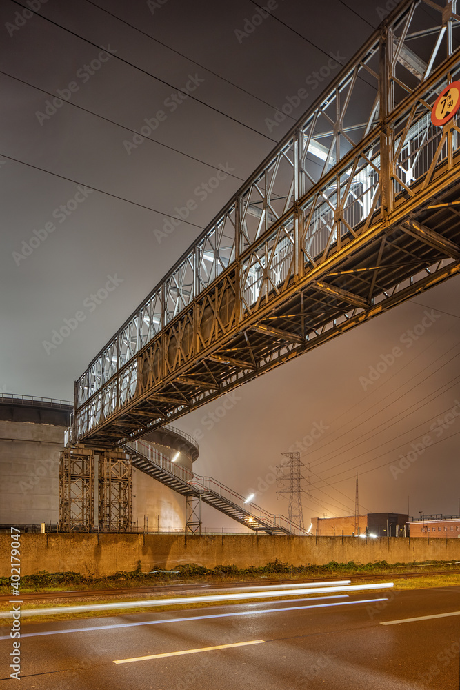 Night scene industrial area with illuminated pipeline overpass, port of Antwerp, Belgium.