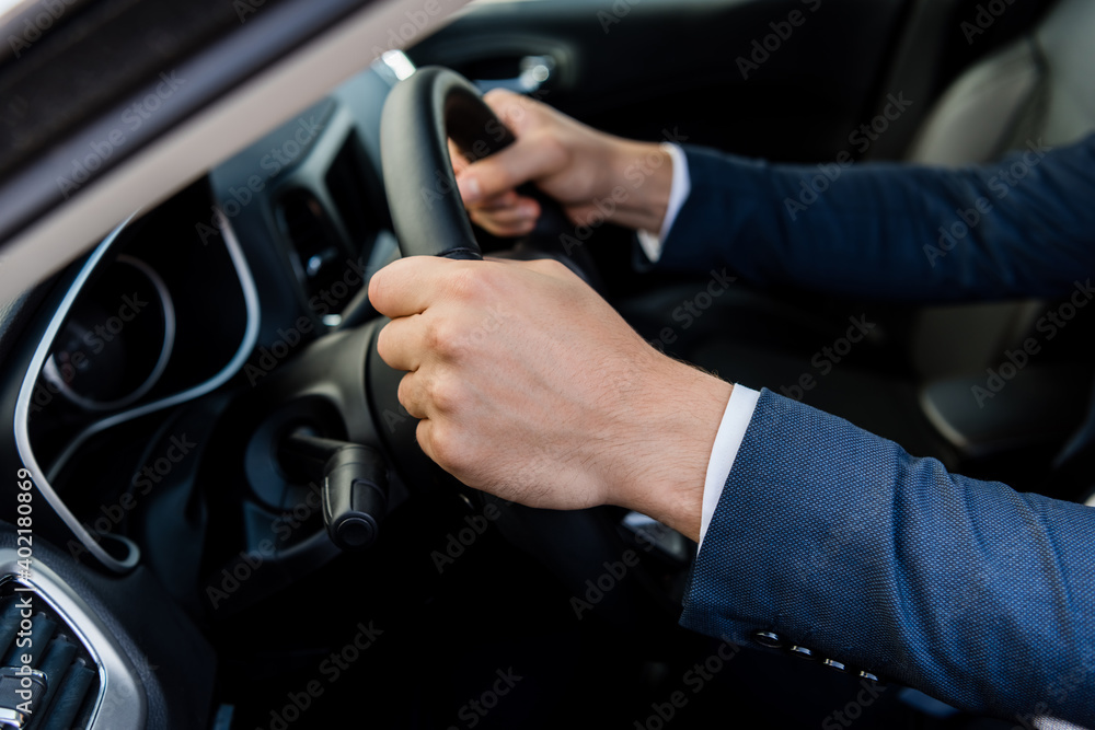 Cropped view of man in suit driving car on blurred background.