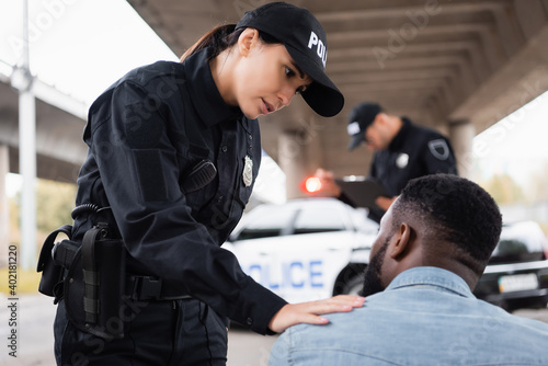 Bild auf Leinwand Policewoman calming african american man near colleague on blurred background on urban street