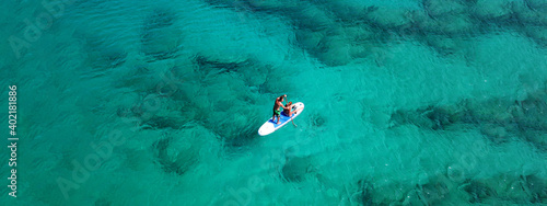 Aerial drone ultra wide photo of couple practice SUP or Stand Up Paddle board in tropical exotic bay with turquoise sea