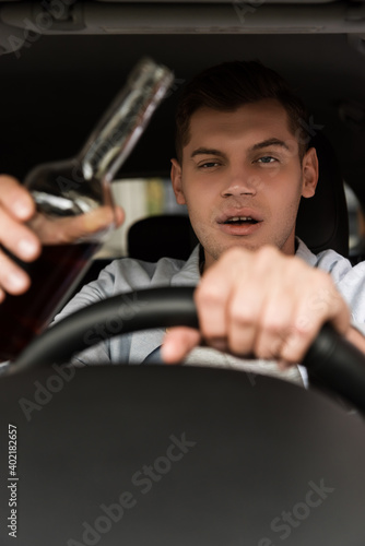 drunk man driving car while holding bottle of alcohol, blurred foreground. photo