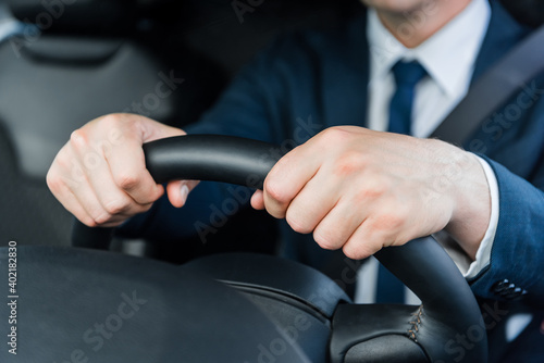 Cropped view of hands of businessman on steering wheel in car.