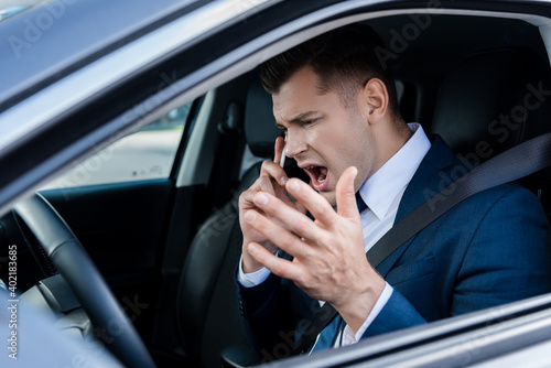 Angry businessman talking on smartphone in car on blurred foreground. © LIGHTFIELD STUDIOS