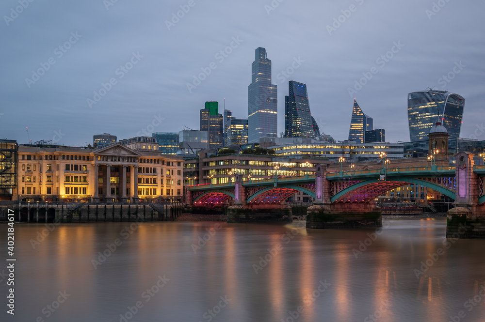 A view of the City of London, at dusk, from the south side of the River Thames, across Southwark Bridge.
