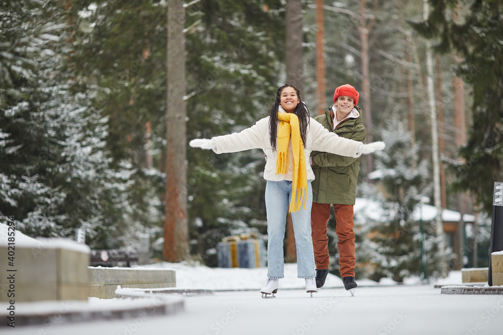 Young happy couple skating together outdoors and enjoying the winter holidays