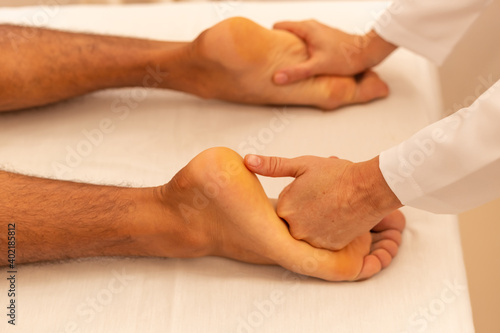 Close em mãos de massoterapeuta aplicando massagem em pé de paciente.