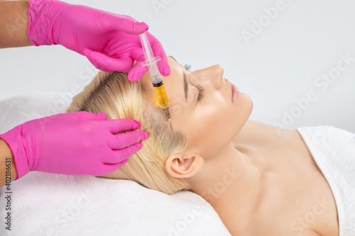 Cosmetologist does prp therapy against hair loss and anti-dandruff of a beautiful brunette woman in a beauty salon. Aesthetic cosmetology concept, hair treatment.