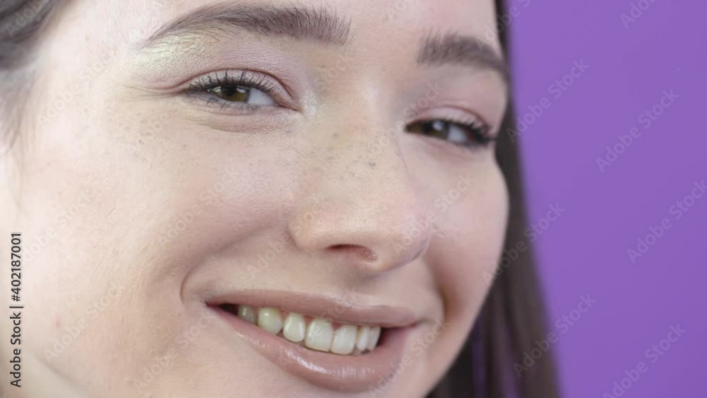 Female model gently stroking hair behind ear while smiling, purple background Female model gently stroking hair behind ear while smiling, purple background