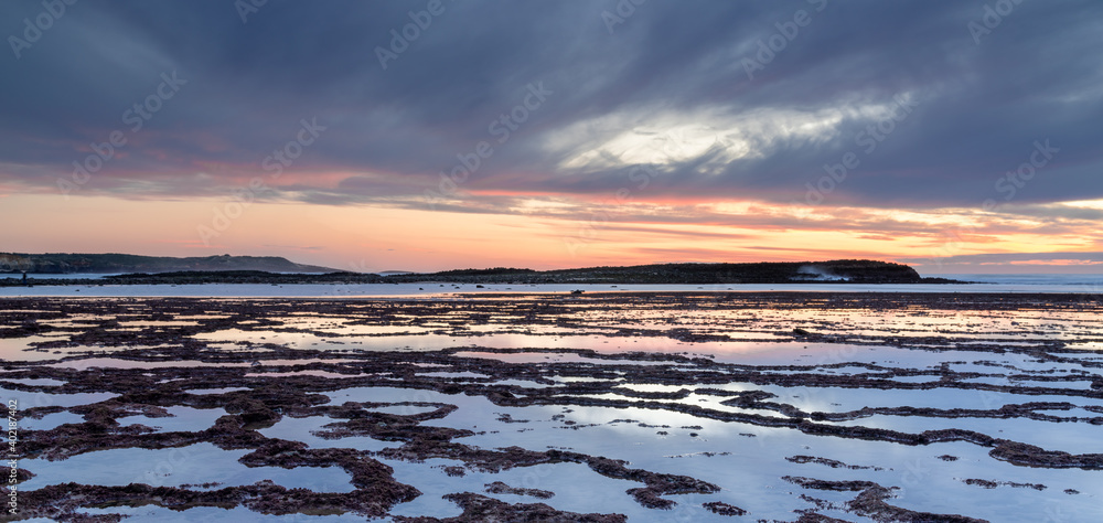 beautiful panorama sunset over the ocean with rocky beach and tidal pools in the foreground