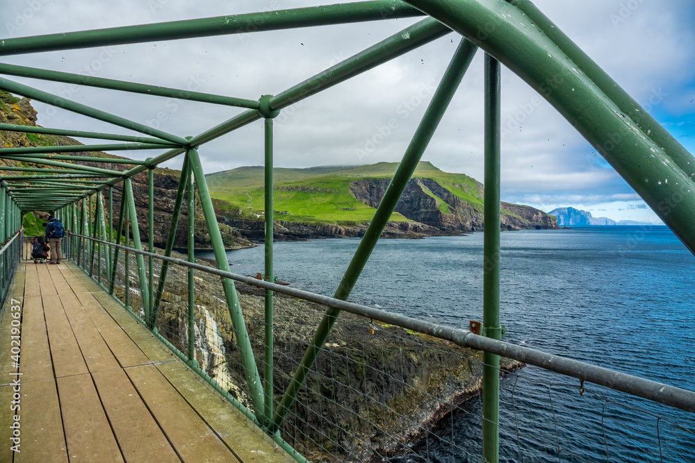 Obraz premium Iron bridge in the Mykines island with unrecognizable tourists