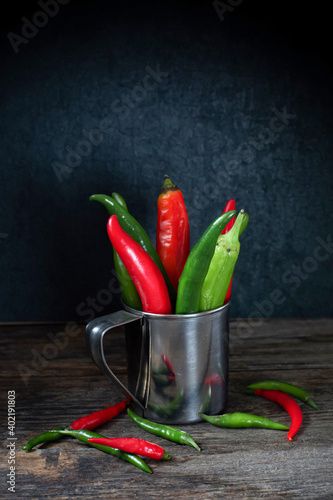 Assorted green and red hot chili peppers in metal dishes stand on a wooden table in the dark. Rustic. Copy space. Vegetarianism.