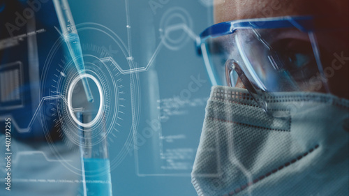 Close-up side view of lab scientist in safety goggles and mask. Concept of developing efficient anti-viral medication, anti-coronavirus vaccine or treatment. Incorporated futuristic graphic interface