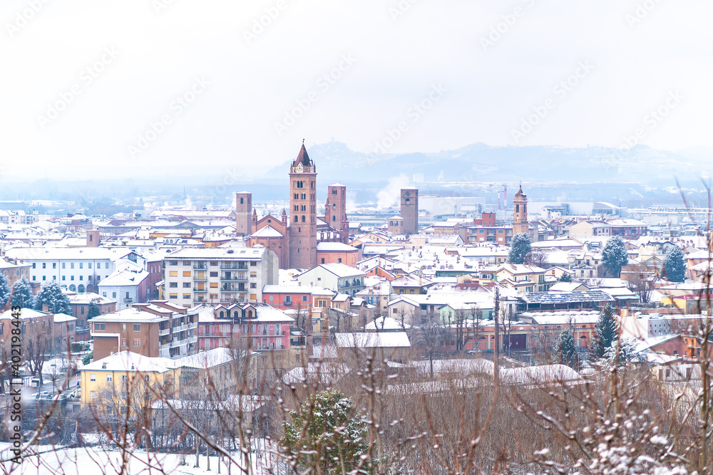Obraz premium View of small medieval Alba town and vineyards on the hills covered in snow in Piedmont, Northern Italy. Langhe wine truffle region. 