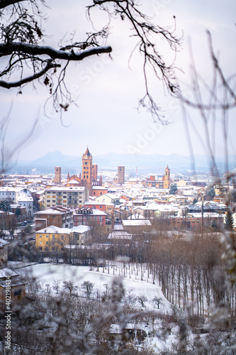 View of small medieval Alba town and vineyards on the hills covered in snow in Piedmont, Northern Italy. Langhe wine truffle region. 