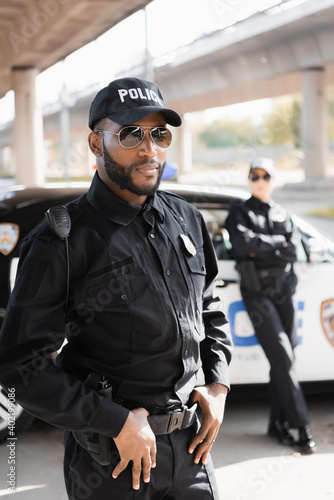 Fotografie, Obraz confident african american policeman looking at camera on blurred background on urban street