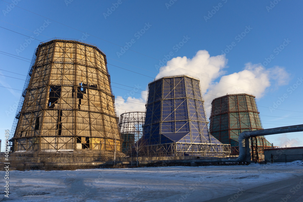 Old destroyed cooling tower and two operating cooling towers. An unfinished cooling tower next to two completed ones. Cooling towers let off steam against the blue sky. Industrial landscape.