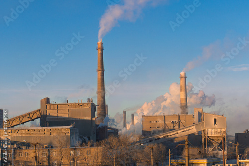 Smoking chimneys of a factory on a background of blue sky. Air emissions, environmental pollution. Industrial building with smoking chimneys.