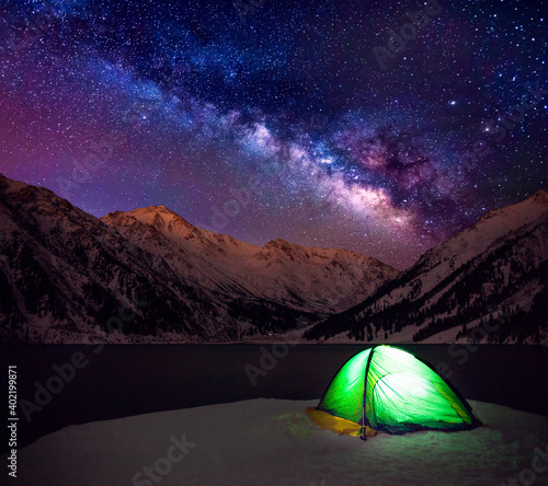 Fototapeta Naklejka Na Ścianę i Meble -  Tent by the lake on a background of snow-capped peaks and the Milky Way at the beginning of the winter season; romantic atmosphere encouraging to travel, explore and discover