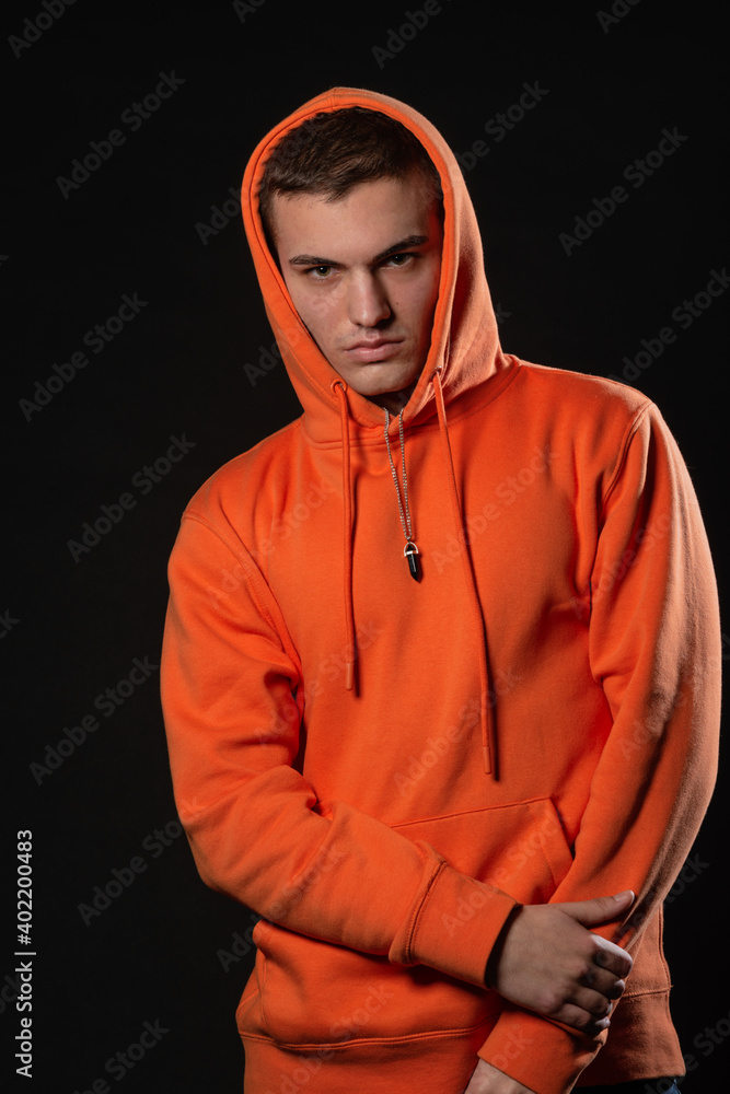 Close up portrait of a handsome male model looking serious while posing in orange hoodie inside a studio