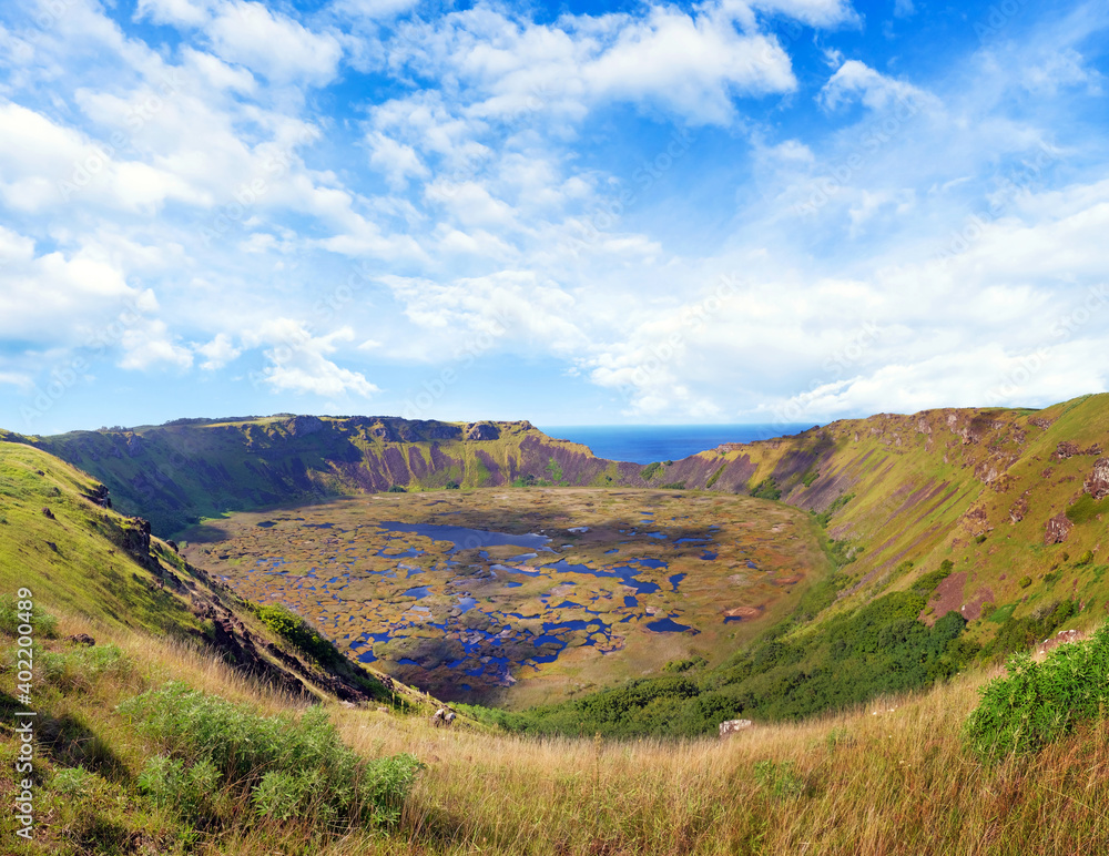 Panoramic view of the Rano Kau volcano on Easter Island - Rapa Nui - against a blue sky, covered by white clouds.