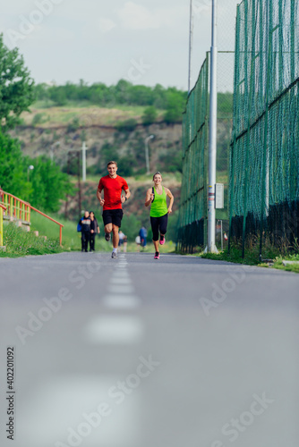 Young male and female athletes jogging and running on a road in the park.
