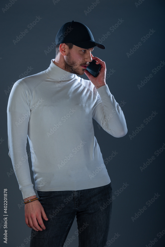 Male model with a black hat and black mobile phone posing in a studio wearing white blouse and black pants Male model with a black hat and black mobile phone posing in a studio wearing white blouse and black pants