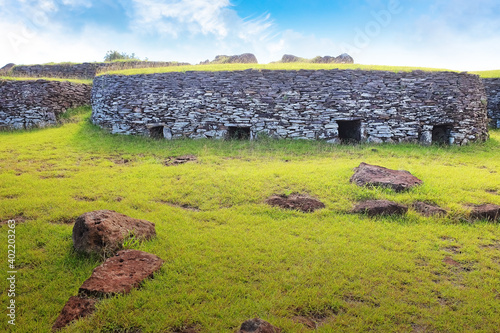 Ruins of the ceremonial village of Orongo, in the archaeological site on the Rano Kau volcano, on Easter Island - Rapa Nui, surrounded by green vegetation, against a blue clear sky.
