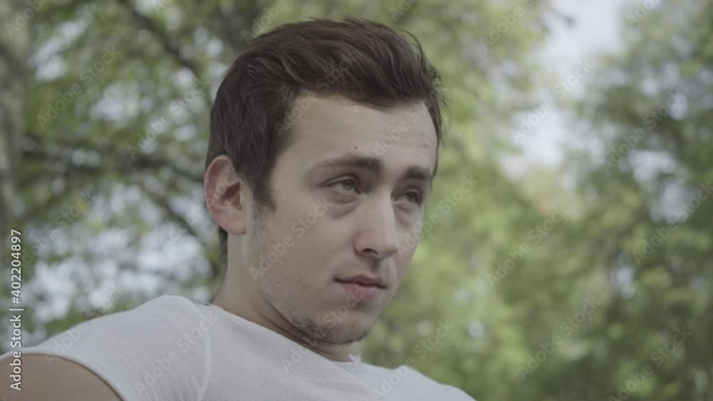 Headshot portrait of thoughtful sad young man sitting in sunny summer park thinking looking away. Close-up of brunette upset Caucasian guy resting alone outdoors. Loneliness and sadness concept. Headshot portrait of thoughtful sad young man sitting in sunny summer park thinking looking away. Close-up of brunette upset Caucasian guy resting alone outdoors. Loneliness and sadness concept.