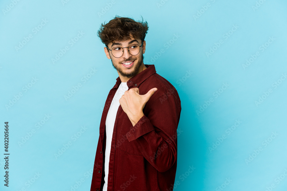 Obraz premium Young arab man on blue background points with thumb finger away, laughing and carefree.