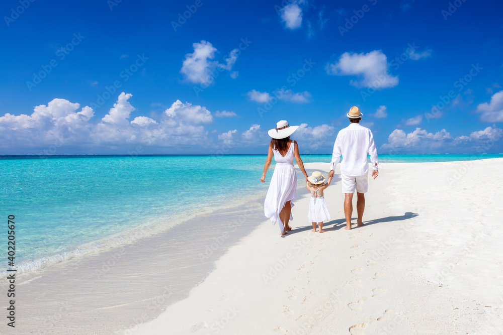 A beautiful family walks together on a tropical paradise beach in the Maldives with turquoise ocean and white sand during their vacation time