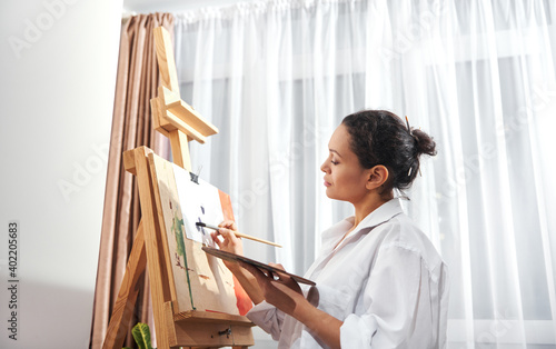Female artist. Brunette woman holding a palette with oil or acrylic paint and painting at home