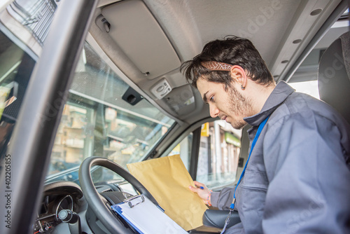 Carrier with uniform in driver's seat looking at the packages to deliver the orders.