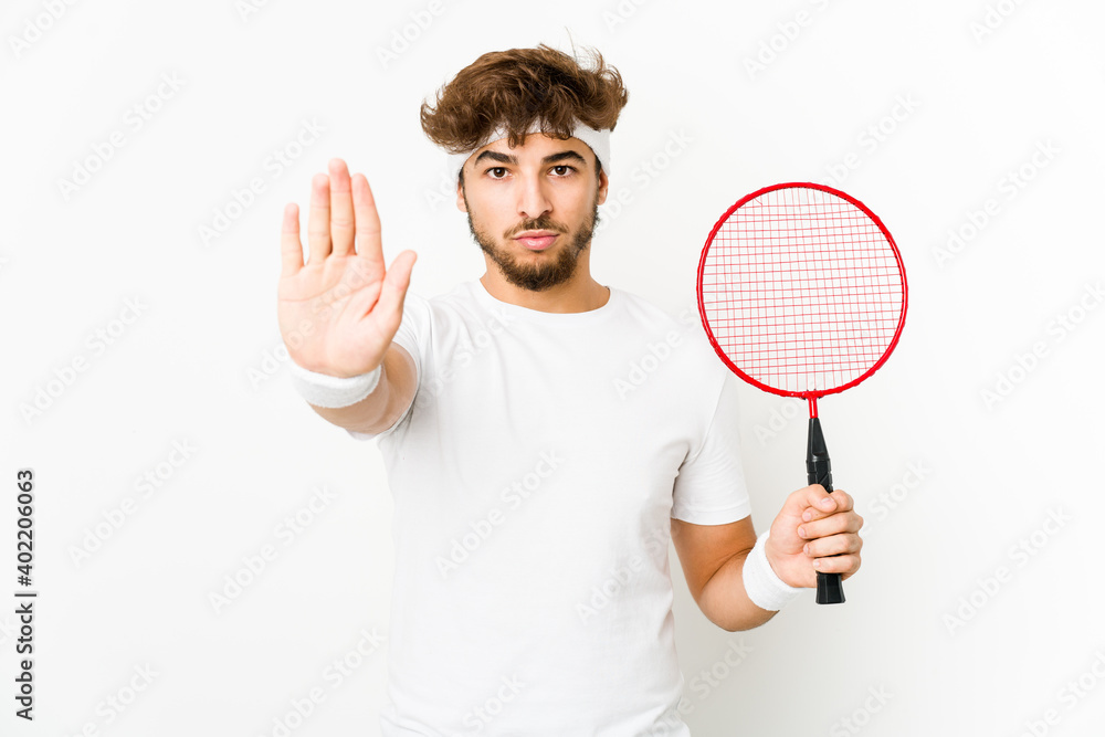 Young indian man playing badminton standing with outstretched hand showing stop sign, preventing you. Young indian man playing badminton standing with outstretched hand showing stop sign, preventing you.