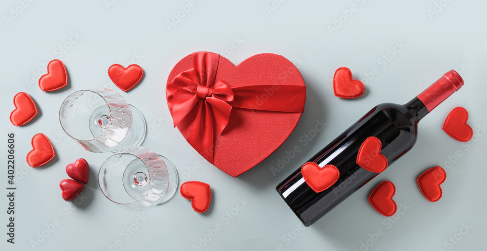 Valentine's Day set for party of red wine and wine glasses and heart gift on blue background. View from above. Flat lay. Romantic greeting card.