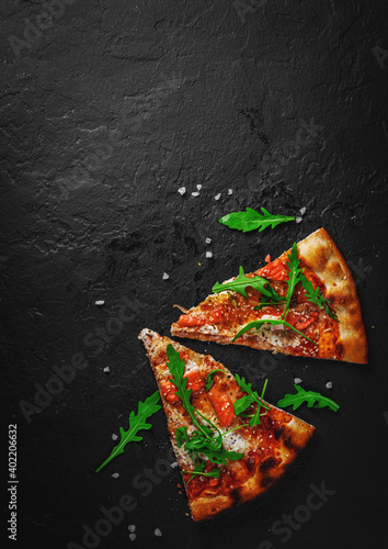 two slice of Pizza with Mozzarella cheese, salmon fish, tomato sauce, arugula. Italian pizza on Dark grey black slate background