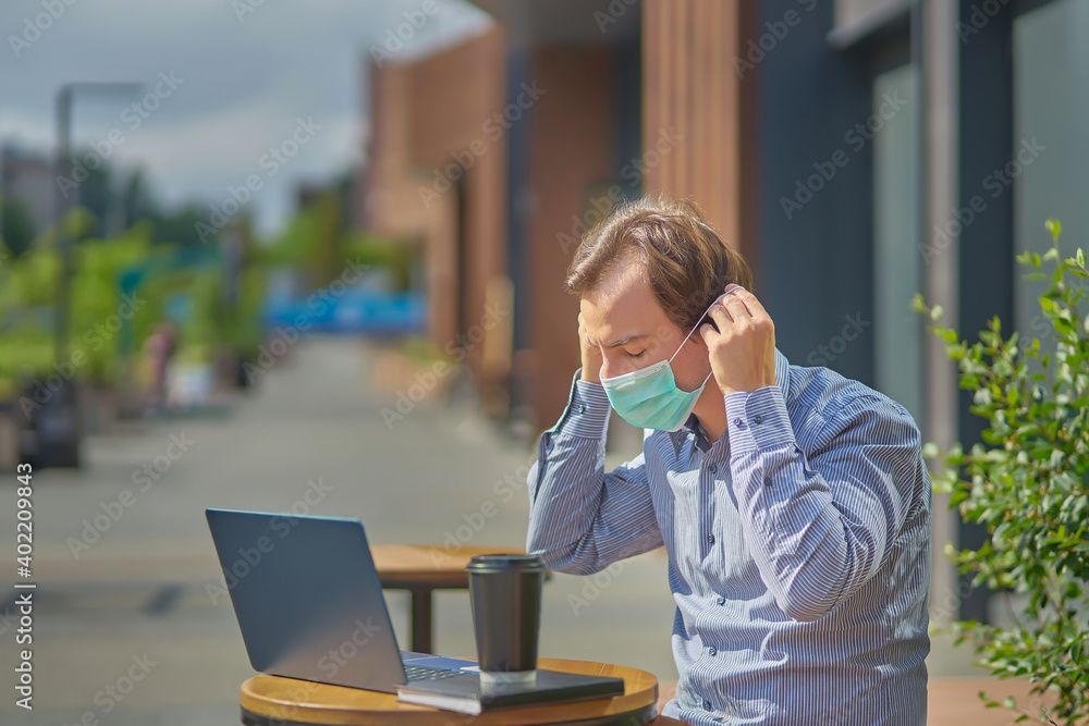 The guy uses a laptop to work outdoors during the coronavirus epidemic. he sits on a bench and puts on a medical mask. The guy uses a laptop to work outdoors during the coronavirus epidemic. he sits on a bench and puts on a medical mask.