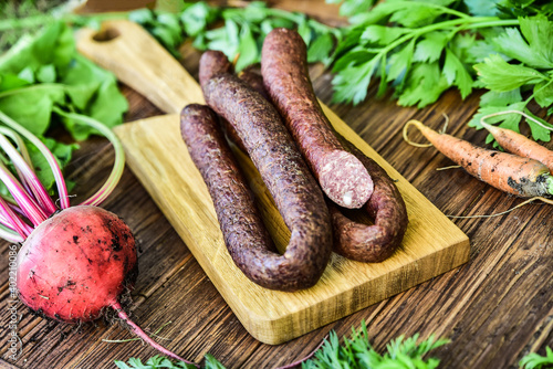 Sausage served on an oak board among vegetables from the home garden.
