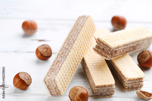 Wafer sticks with hazelnuts on white wooden background