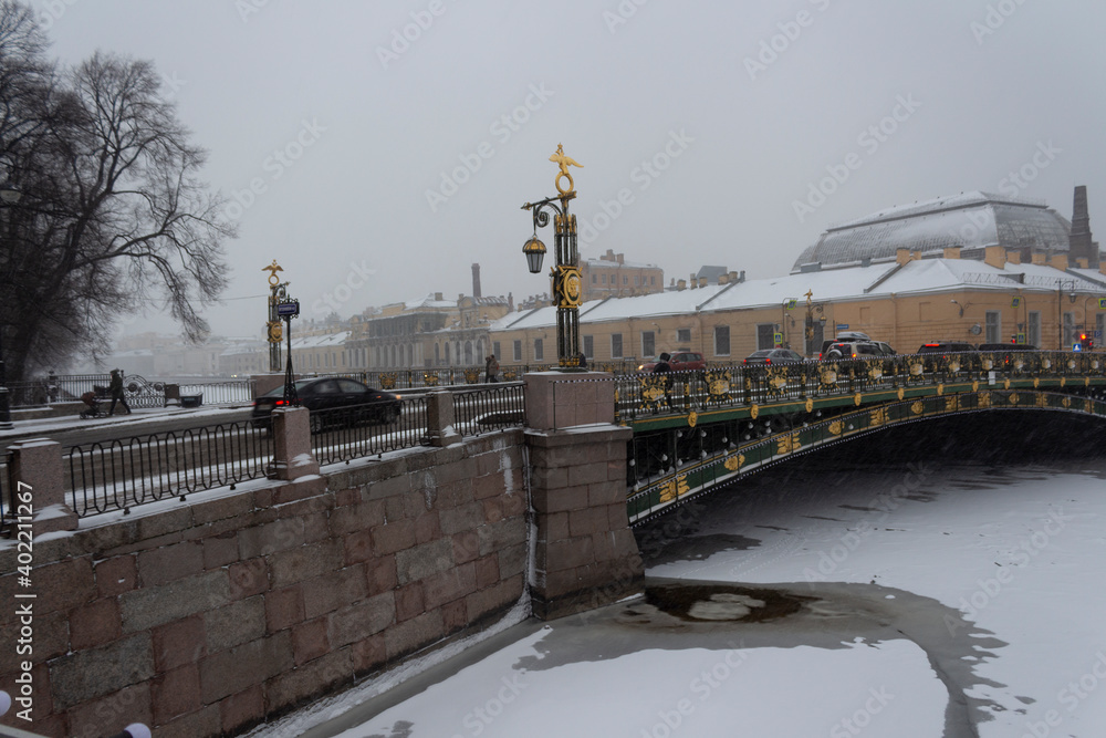 View of the Panteleimonovsky bridge over the snow-covered Fontanka river in St. Petersburg on a snowy and traditionally gloomy day in December. Winter in Russia