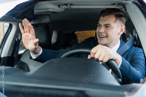 Cheerful businessman waving hand while driving car on blurred foreground. © LIGHTFIELD STUDIOS