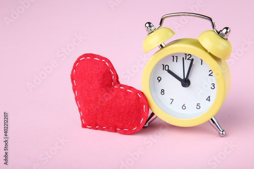 Yellow alarm clock with red fabric heart on pink background