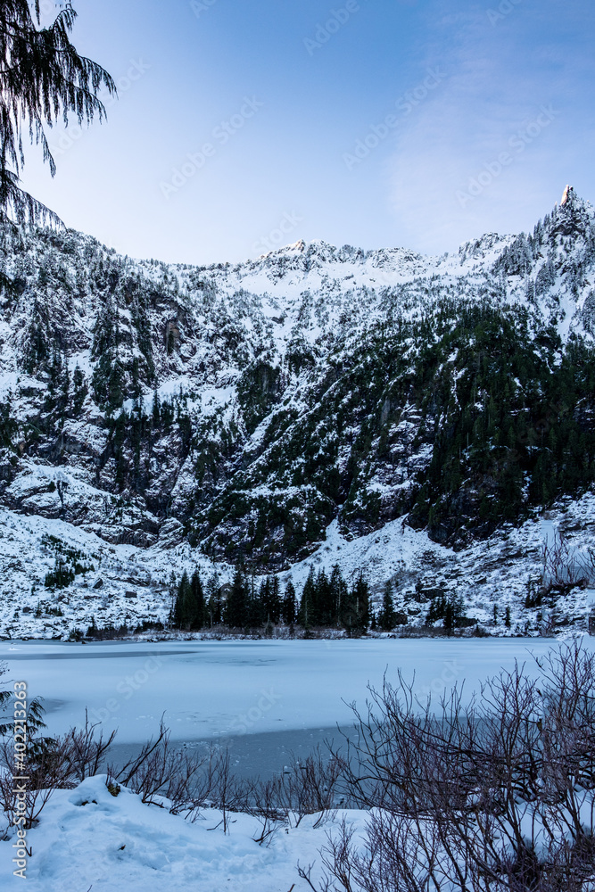 Snow covered cliffs surround a frozen lake with evergreen trees
